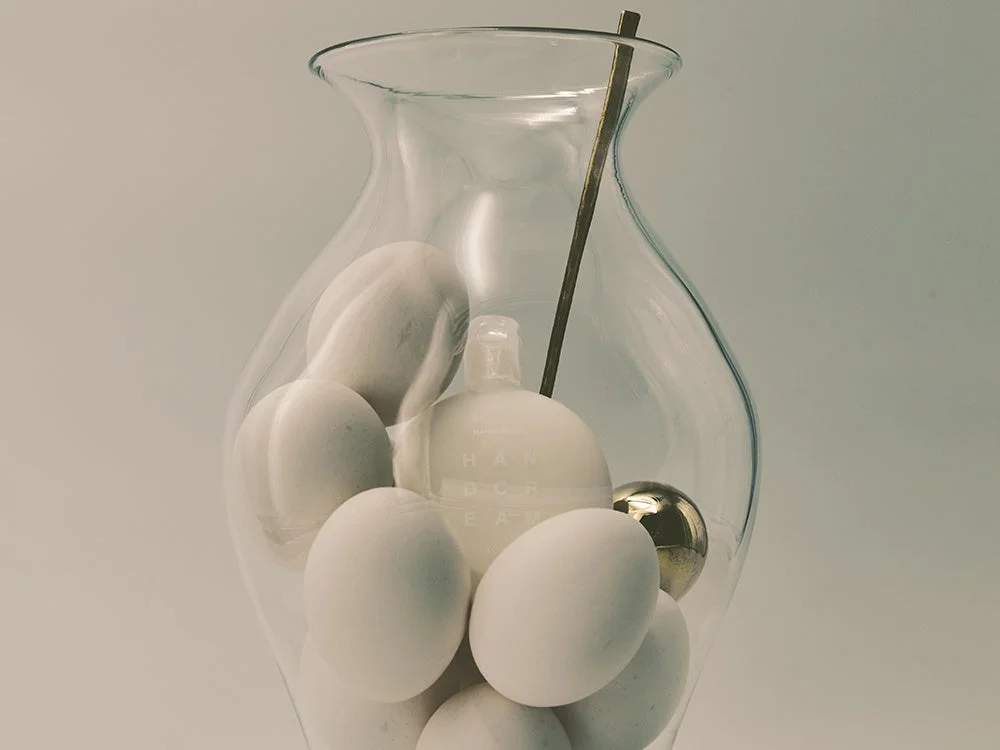 透明なガラスの花瓶に白い卵、白いハンドクリームのボトル、金色の球体