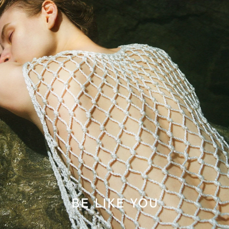 モノクロームの画像で、裸足の人物が草地を走っている様子が捉えられています。動きのある表現で、足元には小さな白い花が咲いています。