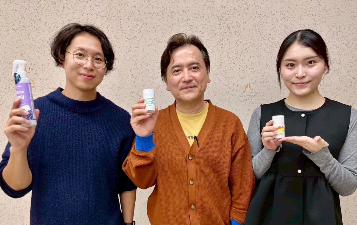 3人の男女が並んで立ち、それぞれ異なる商品を手に持ちカメラに向かって笑顔を見せている様子