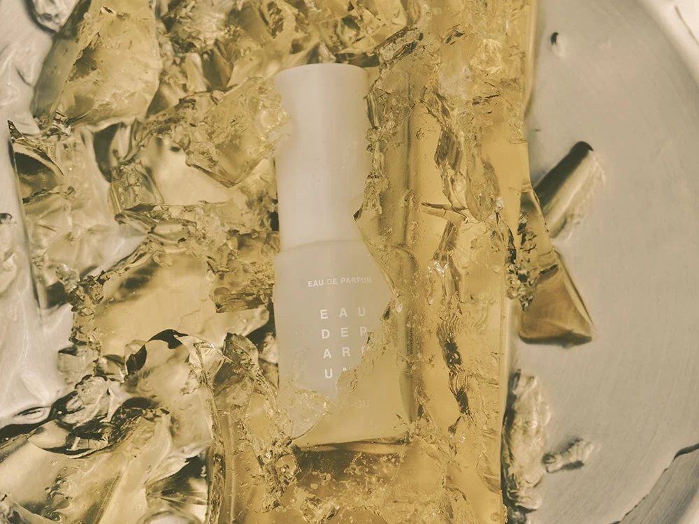 金色に輝く透明なジェルまたは氷のような素材に囲まれた、シンプルな白い香水ボトル