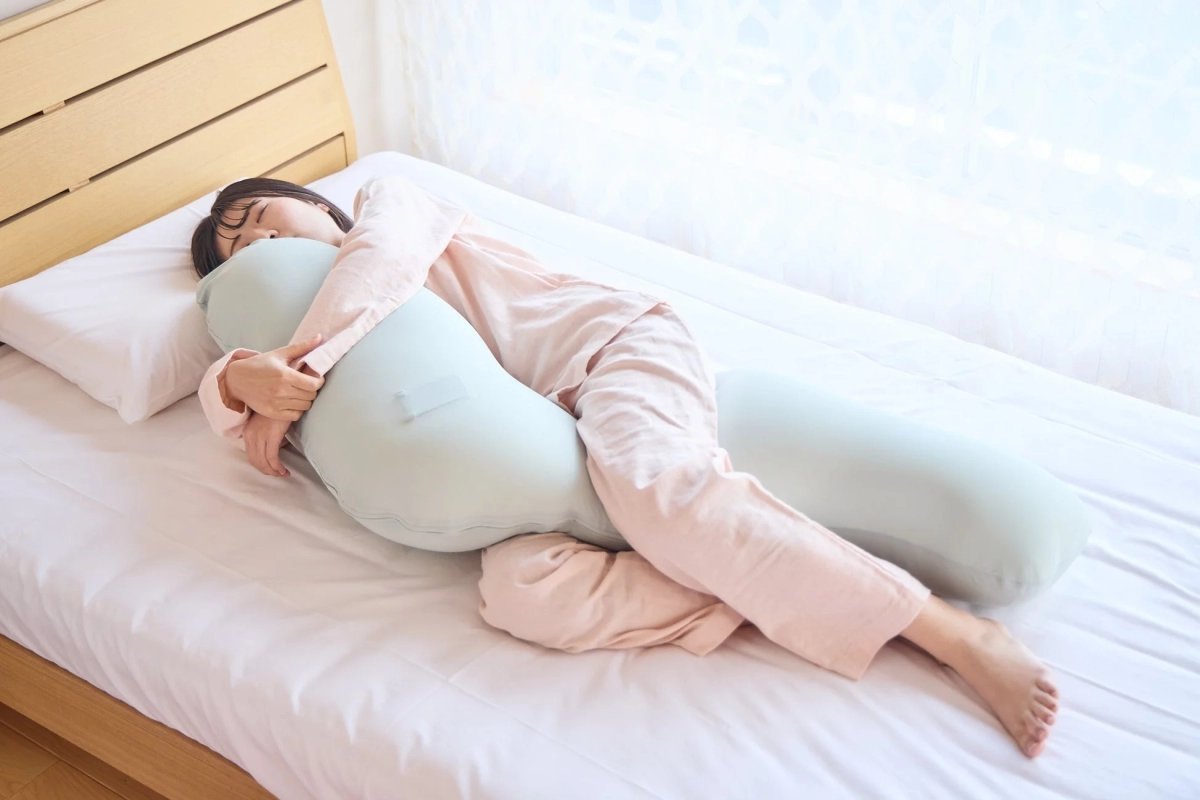 ピンクのパジャマを着た女性が、ベッドで抱き枕を抱きかかえて安らかに眠っています。