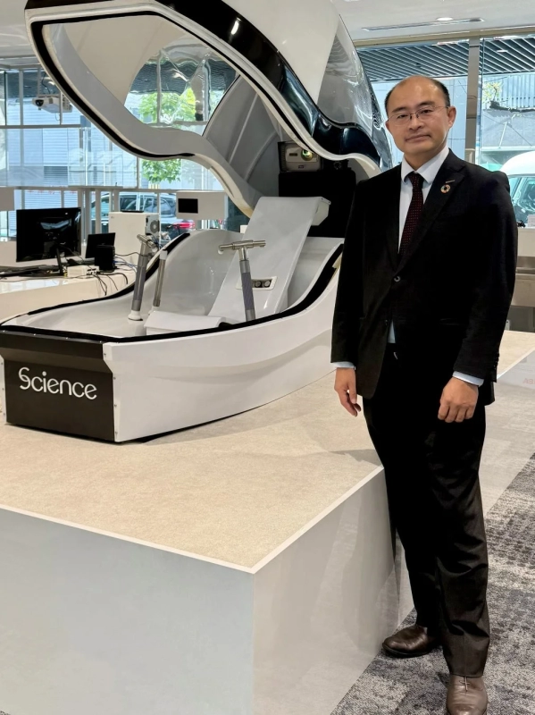スーツを着た男性が、「Science」と書かれた未来的なデザインの白い医療または研究機器の隣に立っている様子。
